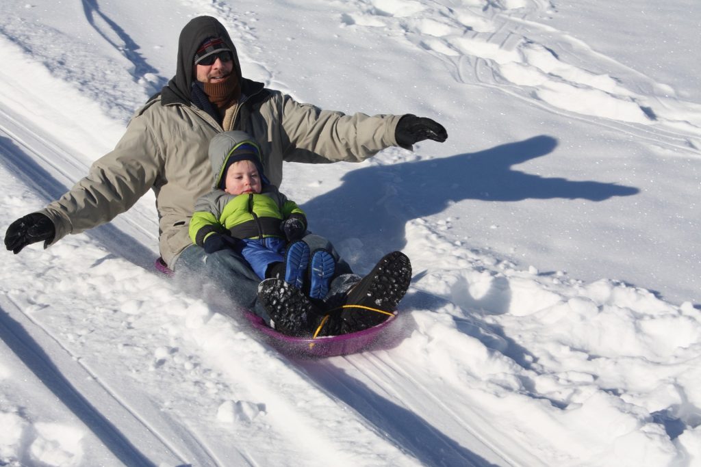 Dad and baby sledding down hill