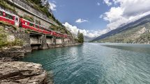 Bernina Express sightseeing train runs past scenic Lake Poschiavo in Switzerland.