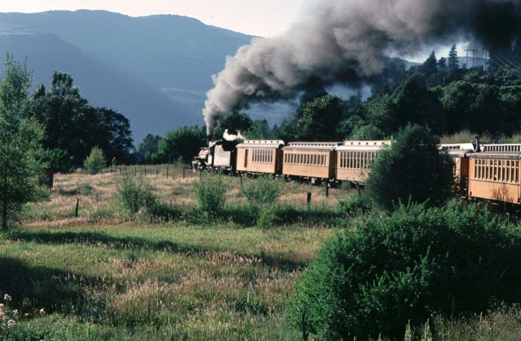 steam train and wooden rail cars travel through countryside