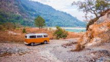 Volkswagen bus parked on unpaved trail near lake.