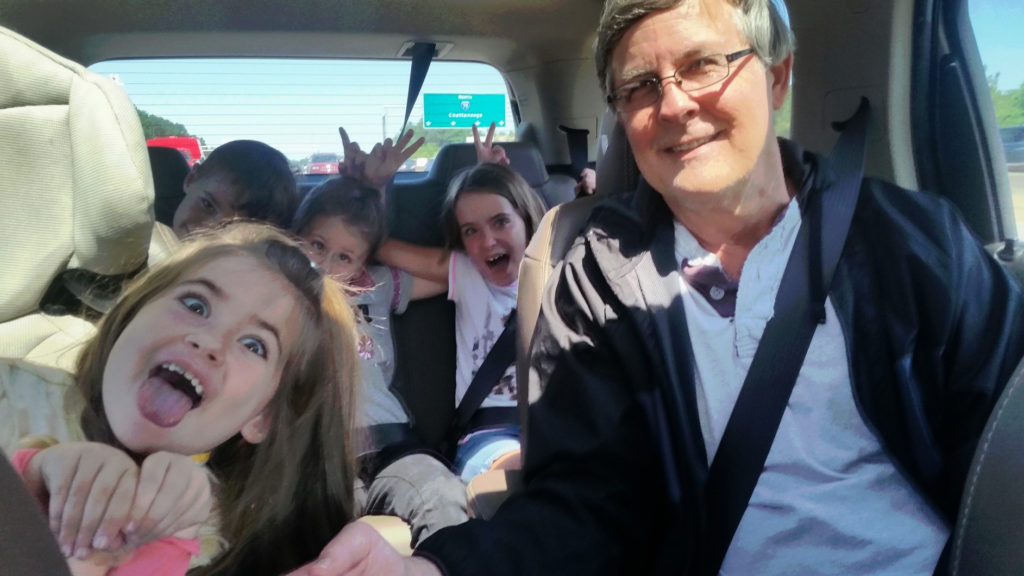 Kids making funny faces while grandpa drives the car on a fall road trip.