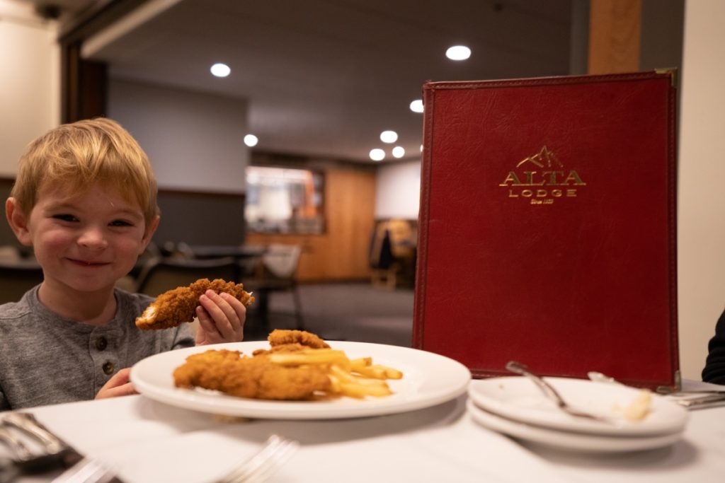 Boy holds chicken finger at dinner table.