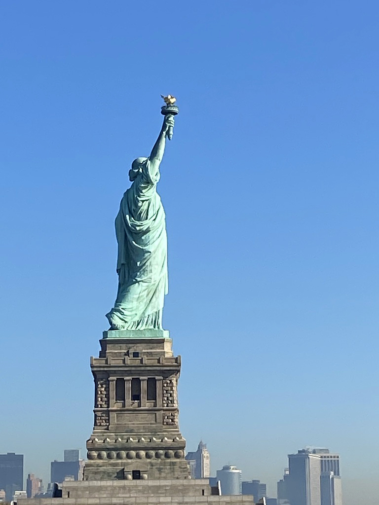 Statue of Liberty seen from behind with New York City skyline.