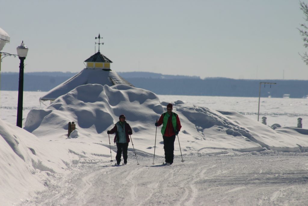 Couples on cross country skis glide past steeple of Mackinac Island church.