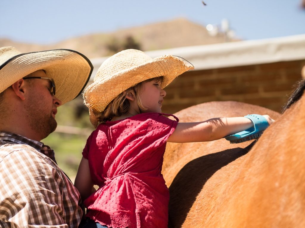 Cowboy holds up a girl so she can groom her horse at Elkhorn Ranch in Arizona.
