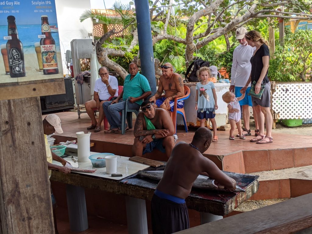 Family watches as local men clean fish at Zeerovers Cafe on Aruba. - traveling to aruba checklist