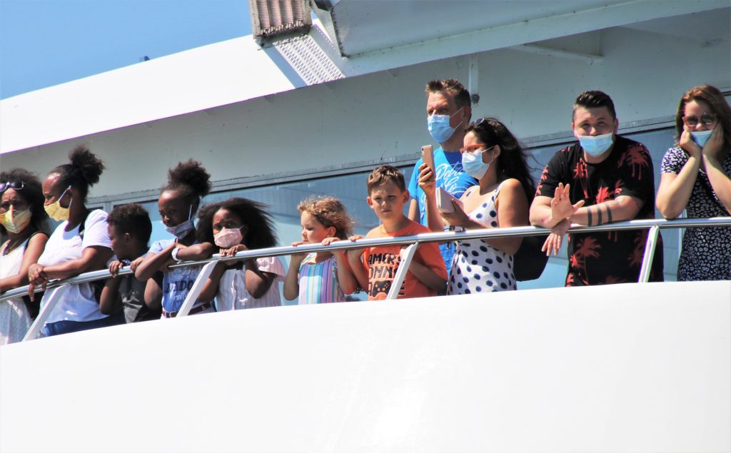 Ferry passengers in face masks stand at railing, ready to set sail