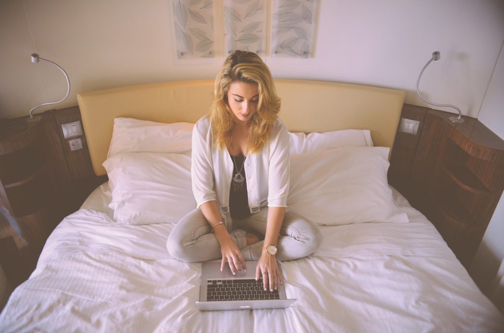 Woman sits on hotel room bed with laptop doing work