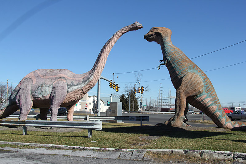 An Apatosaurus approaches a T-rex statue at Dinosaurland in Viginia.