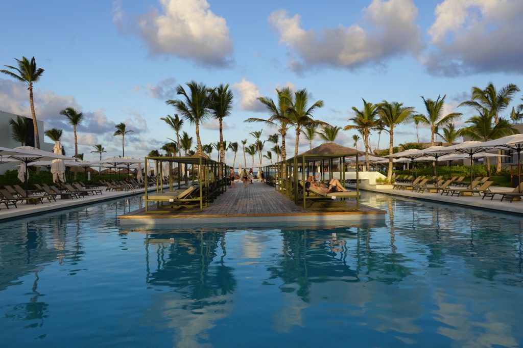 Swimming pool in tropical location with sun loungers on a central deck and around the sides.