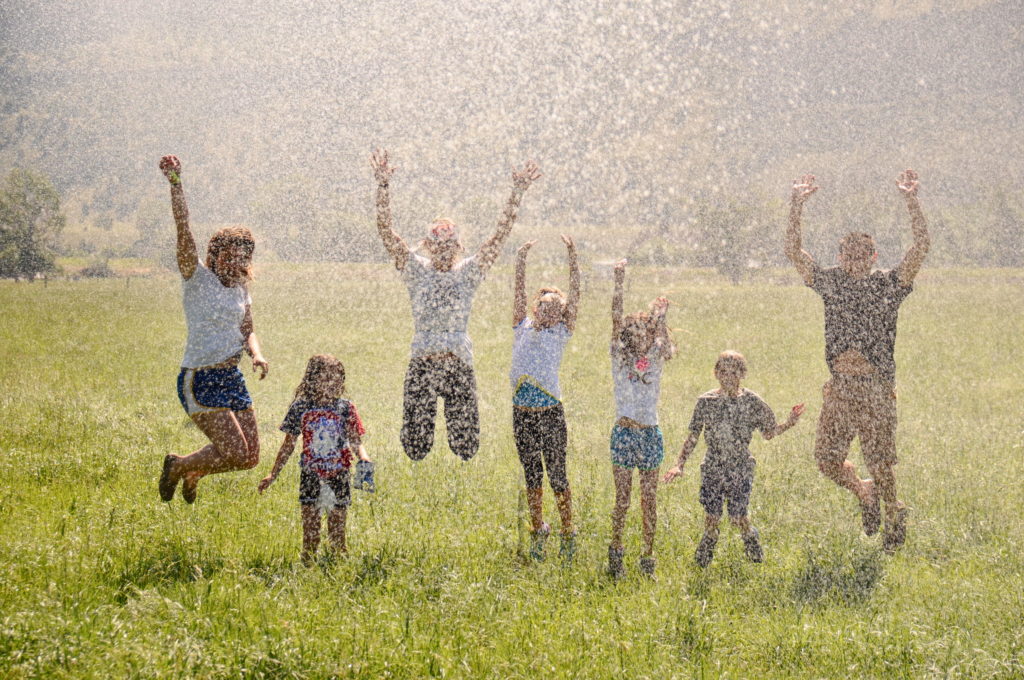 Kids and adults splashing in a water sprinkler at the Mountain Sky dude ranch in Montana.