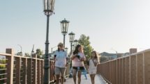 Two women and girl walk across a pedestrian bridge carrying beverages