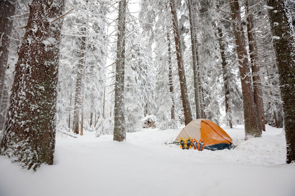 Tent with snowshoes outside the flap in surrounded by a snowy, winter wonderland.