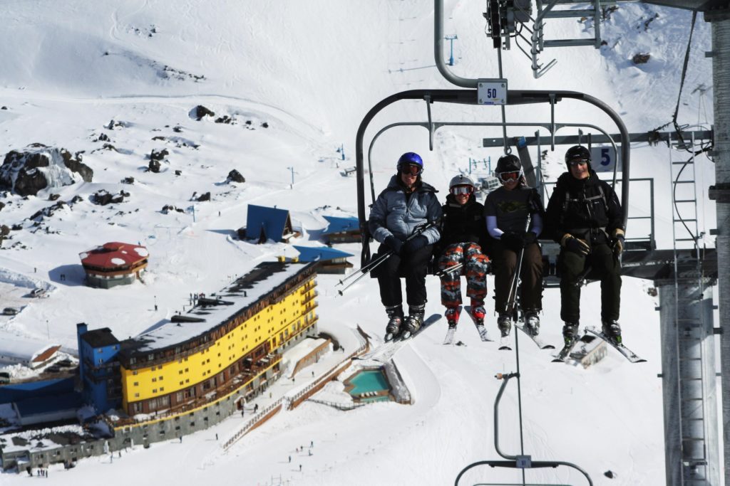 Family in ski gear and coats sitting on a chairlift rising above the ski resort of Portillo in Chile.
