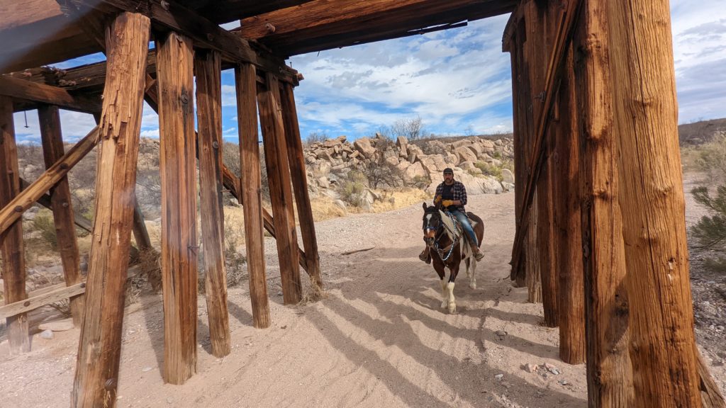 Cowboy rides under old wooden trestle bridge at Monument Tombstone guest ranch in Arizona.