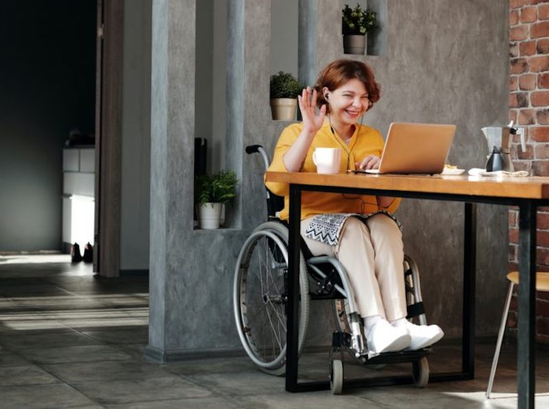 Girl in wheelchair waving at computer screen