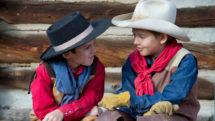 Two boys in cowboy outfits sit and talk.