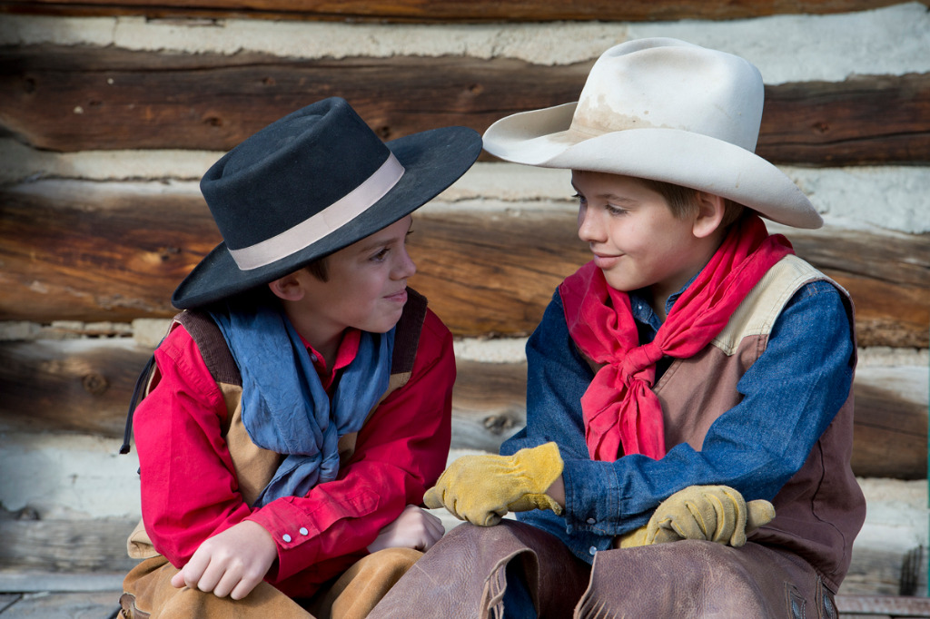 Two boys in cowboy outfits sit and talk.