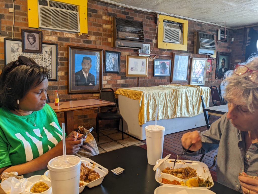 Two women eat fried chicken in takeout containers at restaurant table at Bully's in Jackson, Mississippi.
