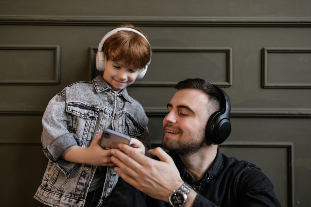 Boy and dad listen to music through headsets while viewing cellphone screen.