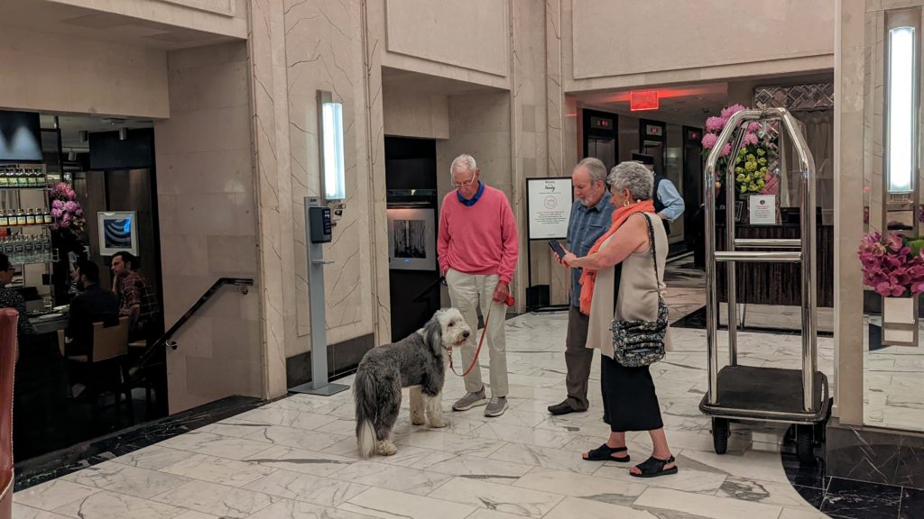 Man with dog stands in hotel lobby while guests take a picture.