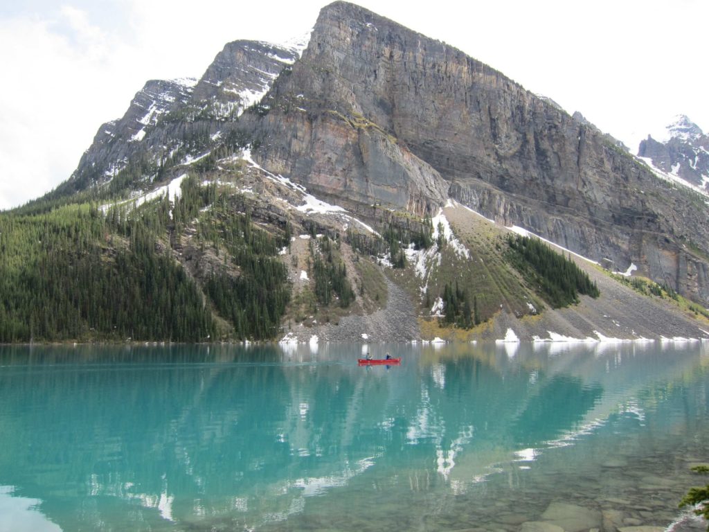 Red canoe on the vivid green-blue water of Lake Louise, Alberta, Canadian Rockies.
