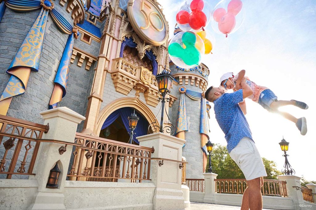 Father and daughter hold ballooons in front of Cinderella Castle, decorated for Walt Disney World 50th Anniversary. Photo c. Walt Disney World Resort