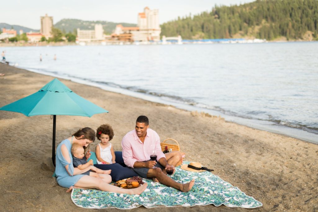 Family on beach blanket sitting on the sand at shore of Lake Coeur d'Alene in Idaho.