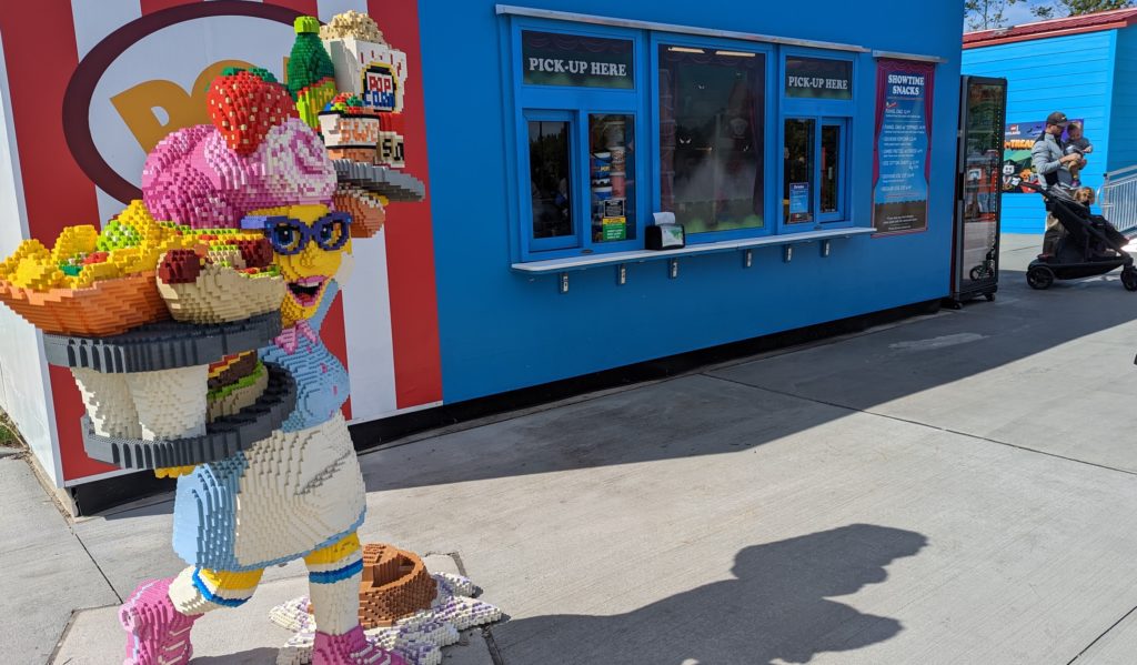 A colorful LEGO waitress made by LEGO Master Builders guides theme park goers to the food concessions.