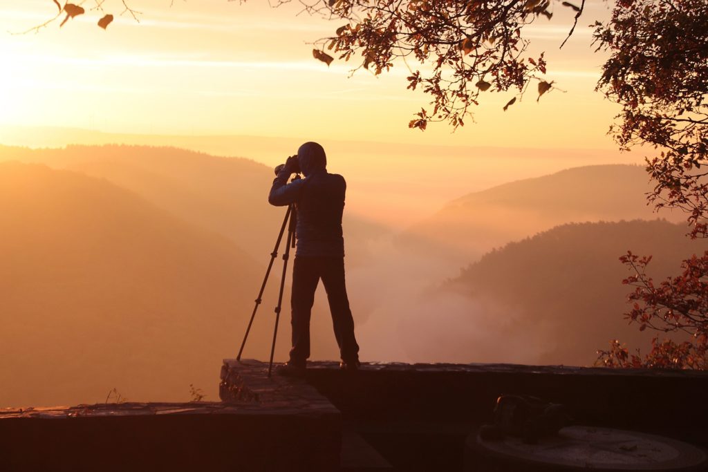 Photographer in silhouette taking a picture of the mountains at dusk.