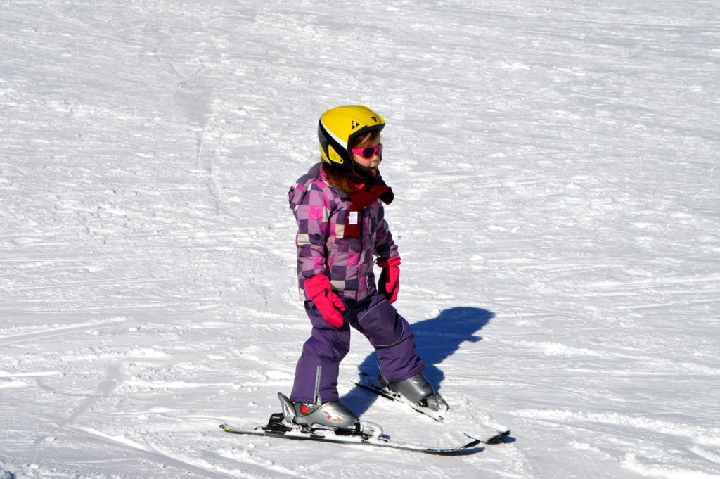 Girl in helmet and ski outfit practices stopping in the snow by making a pizza wedge shape with her skis.