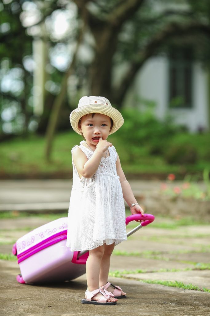 Young girl pulls her own suitcase down path.