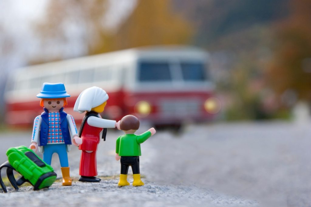 Playmobil figures carry camping gear and point to bus.
