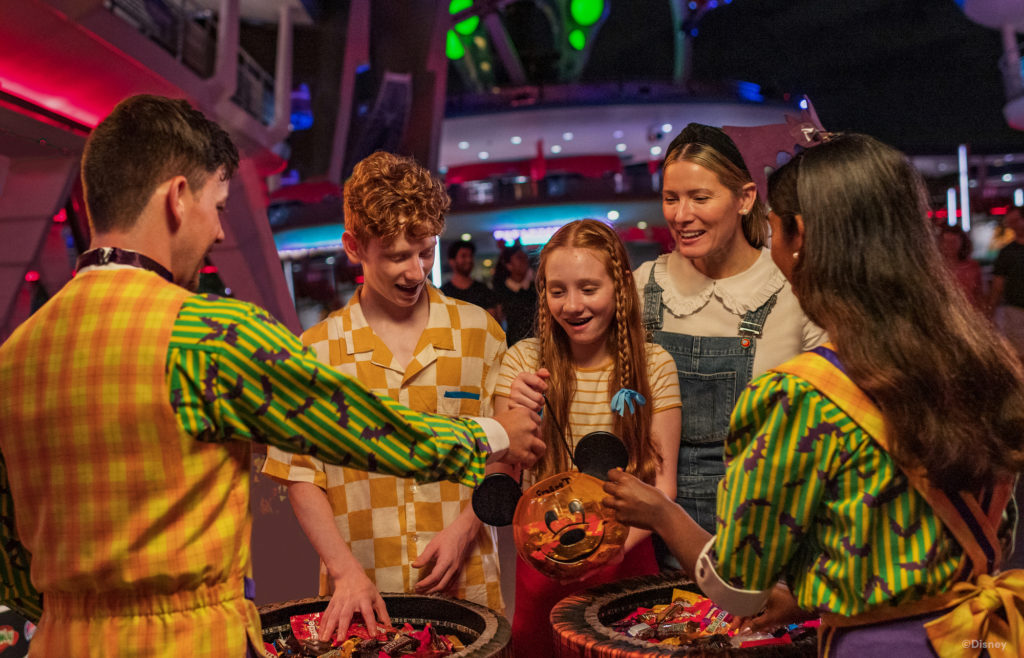 Teens and a woman are getting candy from two costumed actors in a trick or treating event at Walt Disney World.