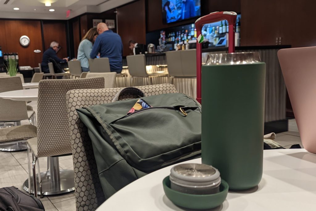 A green Carter Move travel mug by Fellows sits on a table at the United Lounge at AUS airport.