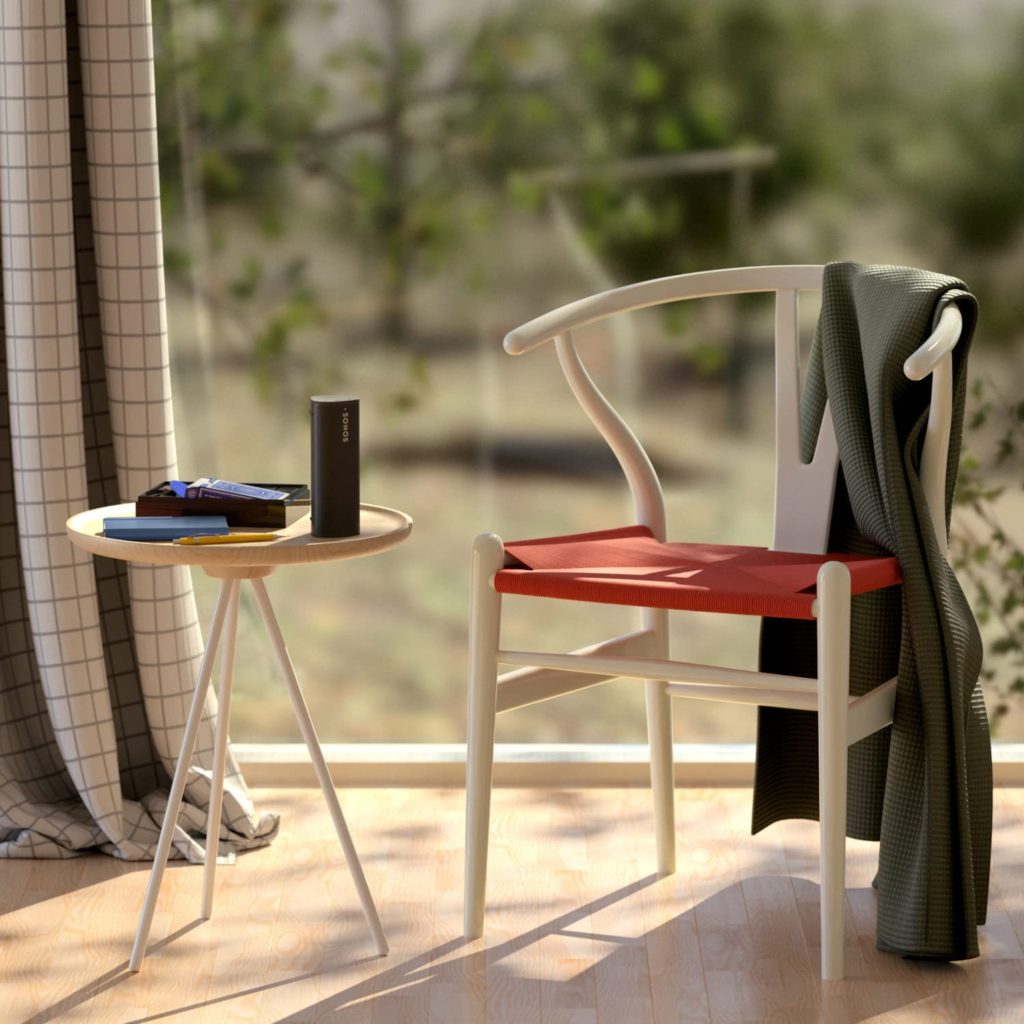 Roam speaker by Sonos on table next to chair, in front of window.