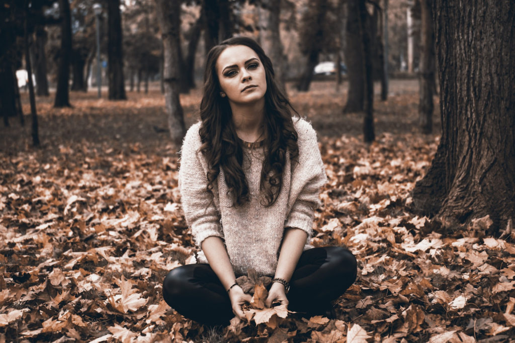 Girl who looks worried sits on pile of leavs in the woods.