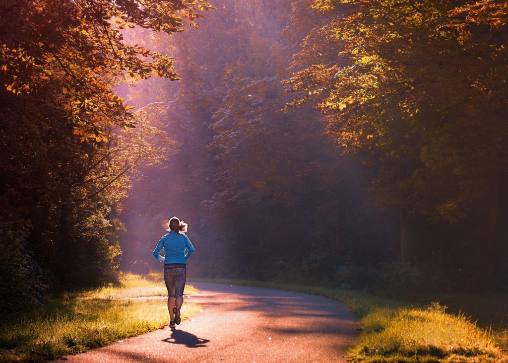 woman on a morning run through the woods illuminated by early sunlight