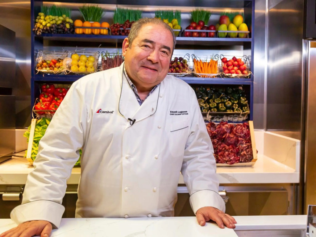 Closeup of Chef Emeril Lagasse in front of shelves of fresh produce.