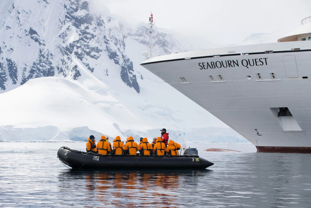 Luxury Seaborun Quest expedition ship with passengers sitting in Zodiac boat exploring coast of Antarctica.