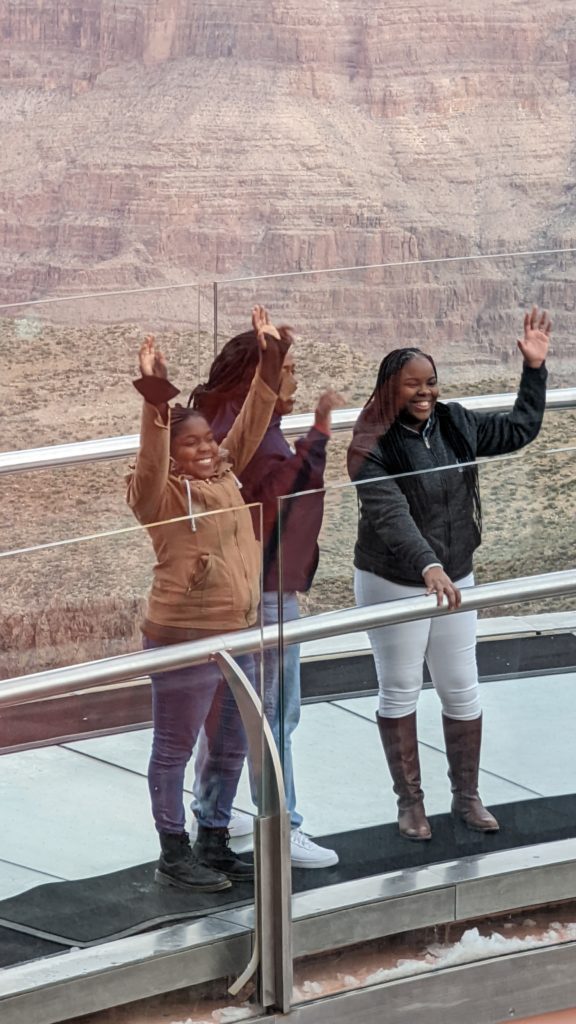 Three women wave to friends from the glass Skywalk that juts out over the Grand Canyon at Grand Canyon West.
