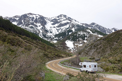 Motorhome parked on side of winding, dirt road leading to snow-capped mountain. By Siggy Nowak for Pixabay.