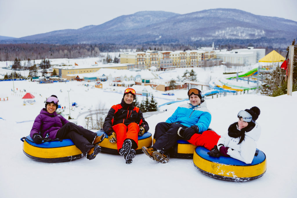 Four adults on inner tubes at top of sledding hill at Village Vacances Valcartier