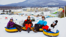 Four adults on inner tubes at top of sledding hill at Village Vacances Valcartier