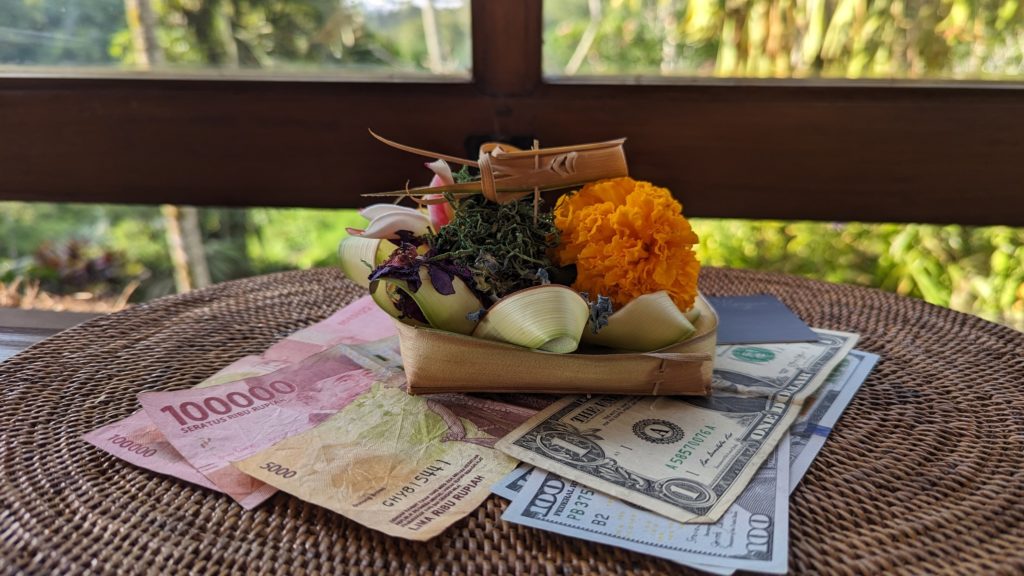 Indonesian rupiah and US dollars sitting on a straw mat with an offering of flowers piled on top.