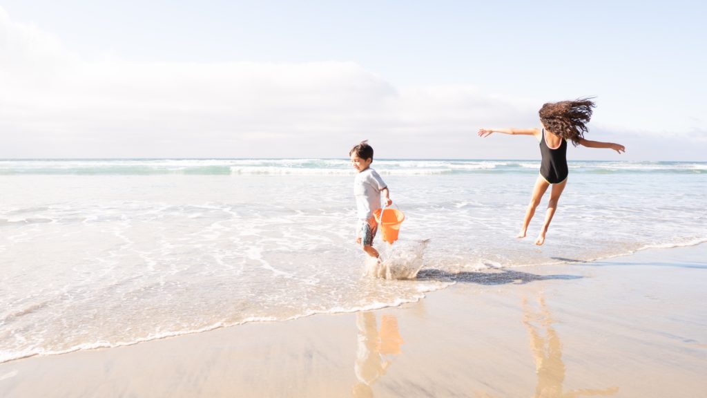 Boy and girl spalsh in the water off of the Nantucket beach. Photo by Garrett Patz for unsplash.