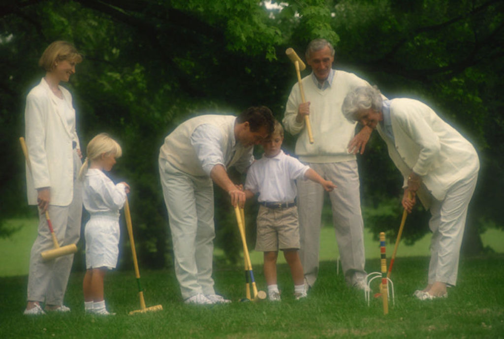 Three generations dressed in white play lawn croquet together.
