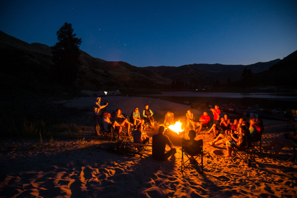 Families sit around a bonfire on the sandy shore of the Salmon River in Idaho.
