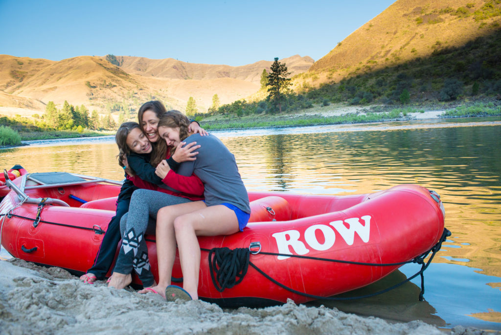 Three girls sitting on edge of an inflatable boat give each other a hug.