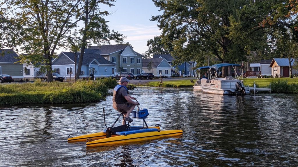 Man on hydrobike paddles in front of homes on a quiet part of the Erie Canal.